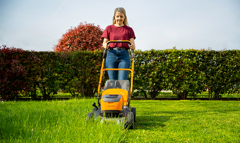 kvinna klipper gräsmatta med batteridriven gräsklippare