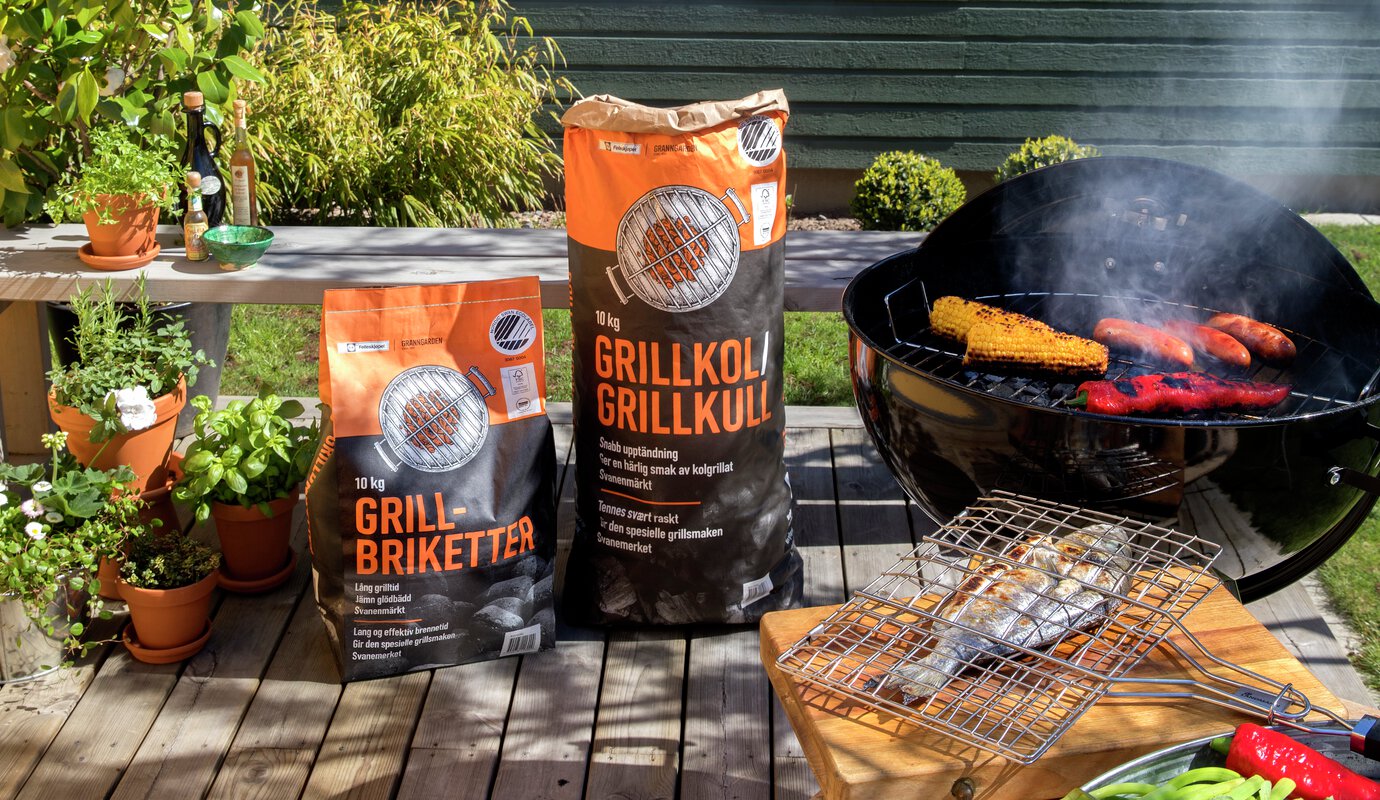 grillplats på trädäck med klotgrill och påsar med grillkol och grillbriketter