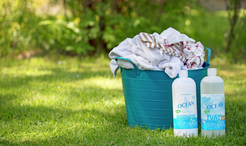 tvättkorg på gräsmattan med tvätt och ocean tvättmedel och mjukmedel/sköljmedel framför i gräset