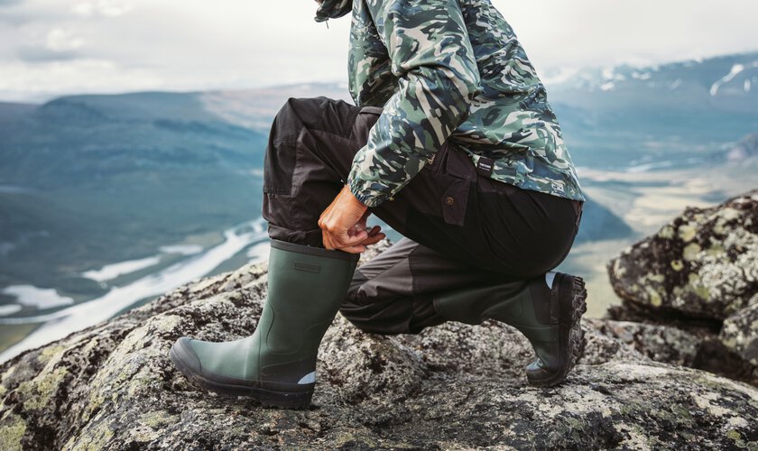 man på huk på bergsklippa som rättar till sina gummistövlar ute på tur