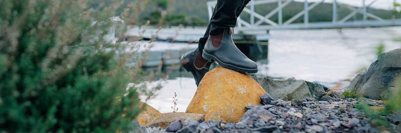 Läderskor på en sten med natur och vatten i bakgrunden